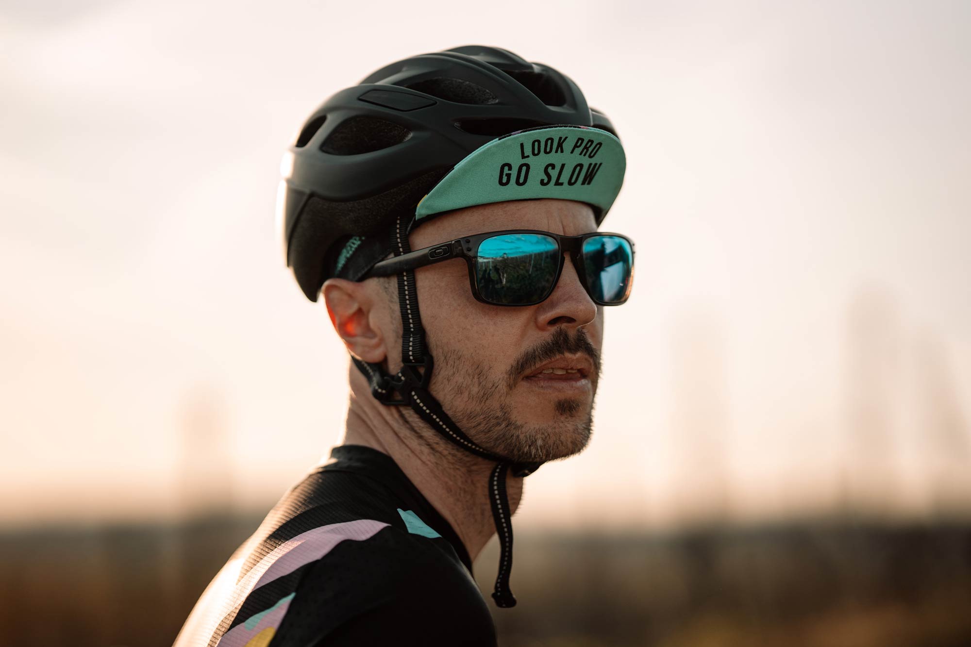 Nahaufnahme Rennradfahrer mit Helm Mütze und Sonnenbrille bei Sonnenuntergang
